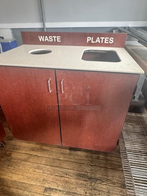 Red wood waste receptacle with a countertop featuring labeled openings for waste and plates. Dual cabinet doors below.