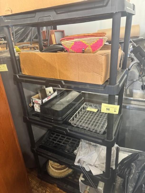 5-tier black plastic storage shelving unit, used condition, with various household items placed on shelves.
