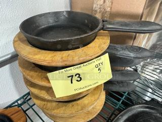 5" cast iron skillet BIDX5 with handle, stacked with wooden trivets, in good condition, auction label indicates quantity 5.