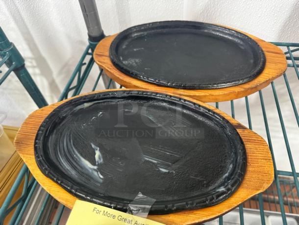 Two oval cast iron skillets on wooden trays, used condition, ideal for serving sizzler dishes.