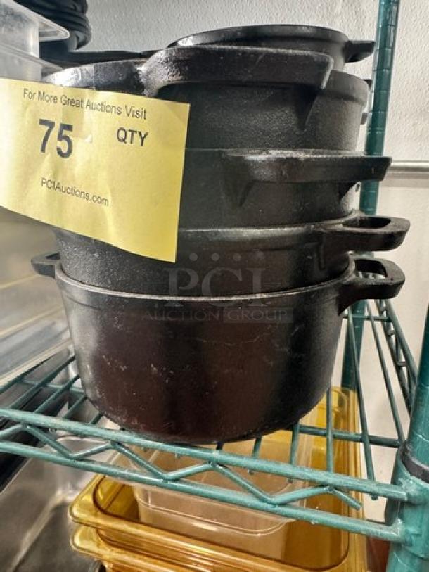 Cast iron small Dutch oven without lid, stacked on shelf, black finish, durable construction, auction tag indicating 75 quantity.
