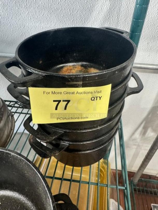Stack of small cast iron Dutch ovens without lids, labeled "77", black, showing signs of use, on metal shelf.