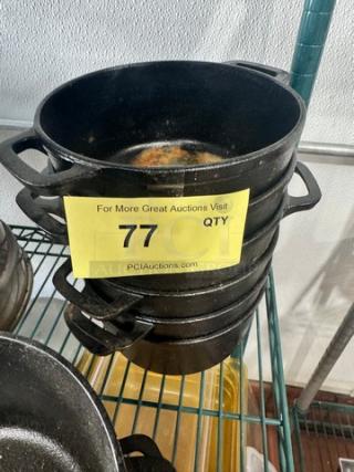Stack of small cast iron Dutch ovens without lids, labeled "77", black, showing signs of use, on metal shelf.