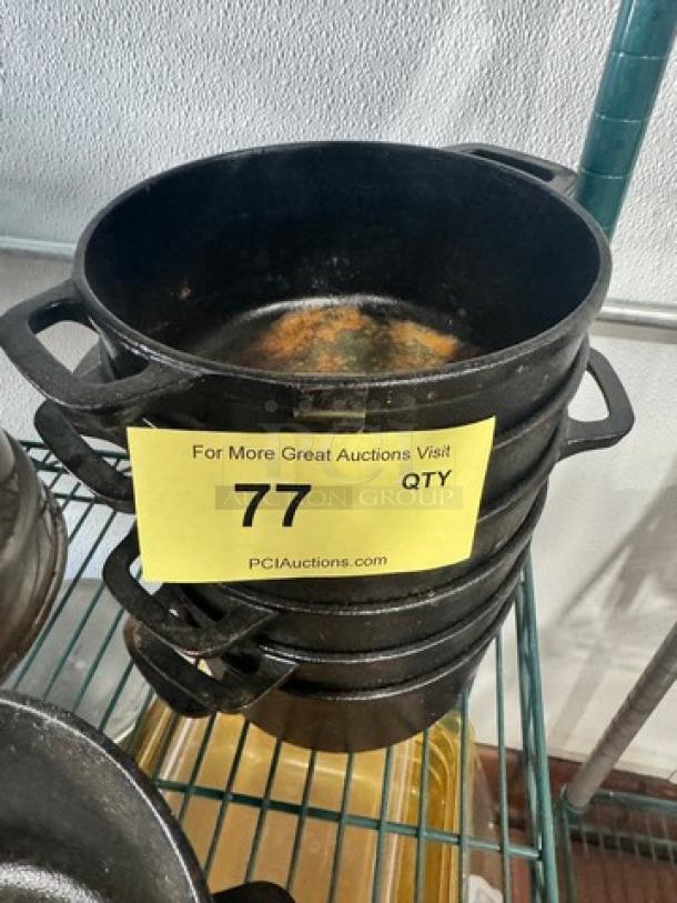 Cast iron small Dutch oven without lid, item number 77, stacked on shelf, used condition, auction label visible.