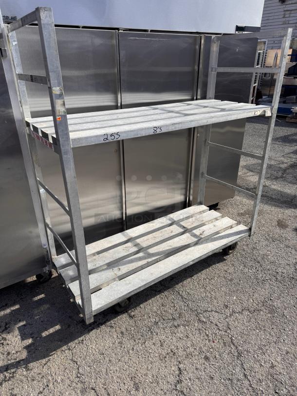 Metal mobile rack with two shelves, wheels for mobility, labeled "255" and "8's", showing signs of wear.