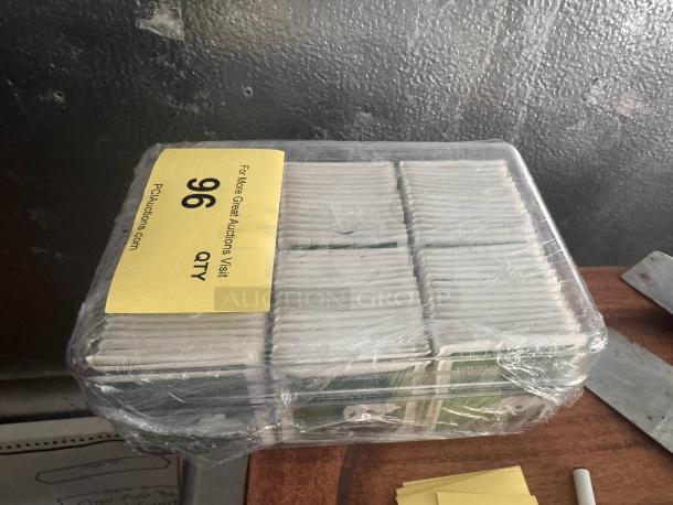 Pack of green tea bags wrapped in plastic, labeled "96 QTY," in good condition, stored on a wooden surface.