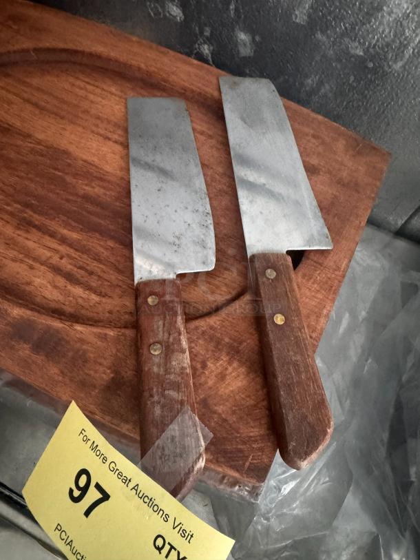 Lot of 2 vintage cleaver knives with wooden handles, showing signs of wear, resting on a wooden surface.
