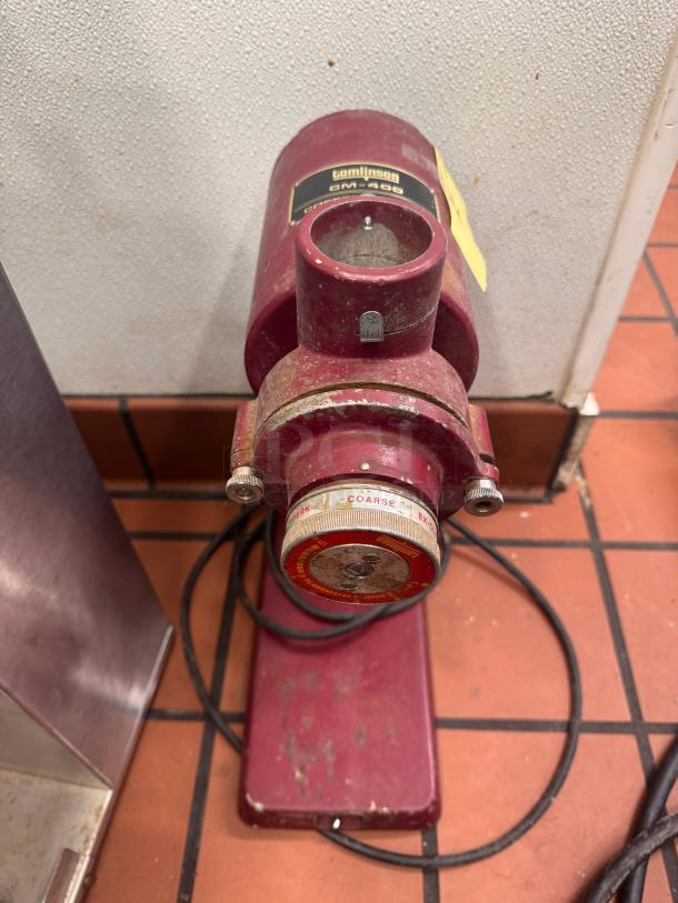 Tomlinson CM-400 commercial coffee grinder, showing signs of wear. Red color, visible settings dial for grind coarseness.