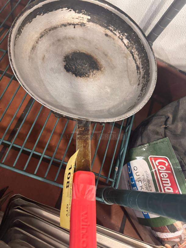 Lot of 2 skillets, worn condition, metal with red handles, Winco brand label visible, auction tag marked "108."