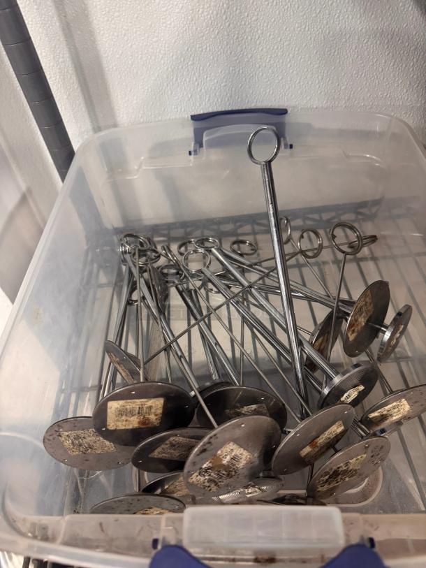 Lot of metal card holders in a plastic bin, featuring circular bases and loop tops. Condition appears used with label markings.