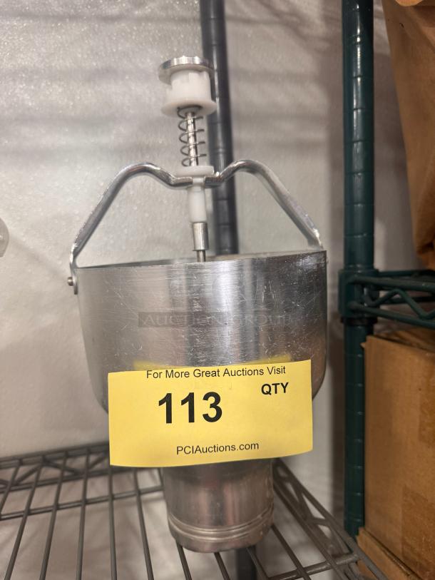 Metal pancake batter dispenser with a plunger mechanism, used condition. Yellow auction tag with "113" and "PCIAuctions.com".