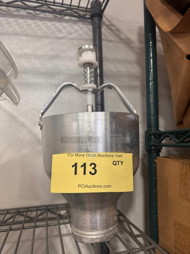 Metal pancake batter dispenser in used condition, with a handle and plunger mechanism. Yellow auction tag with number 113.
