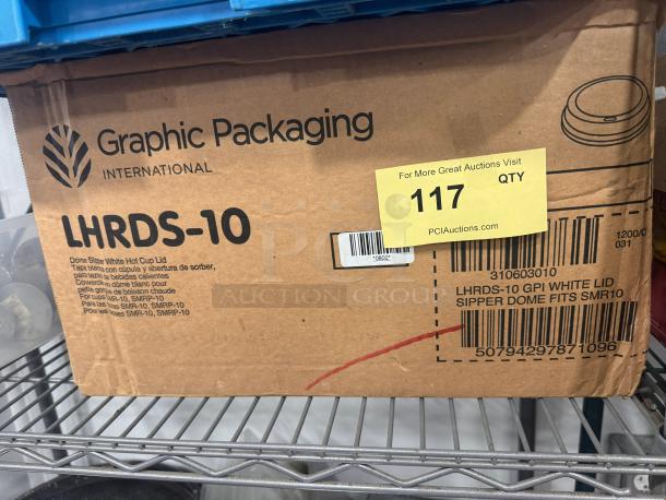 Cardboard box labeled "Graphic Packaging International, LHRDS-10." Contains white hot cup lids. Auction tag "117" visible.