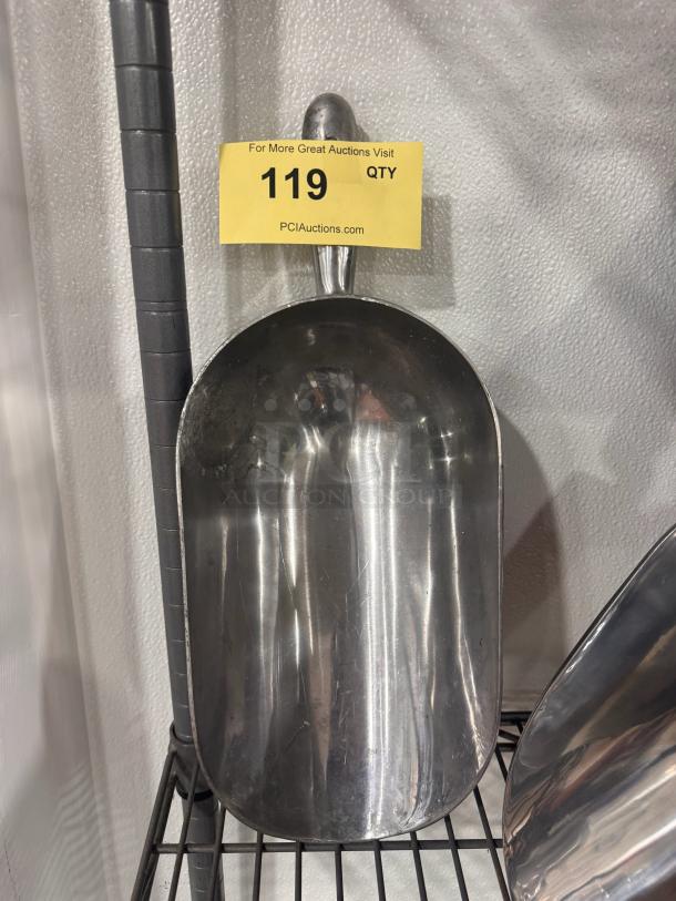 Metal ice scoop with a curved handle, shiny finish, displayed on a wire shelf. Auction tag indicates item 119.