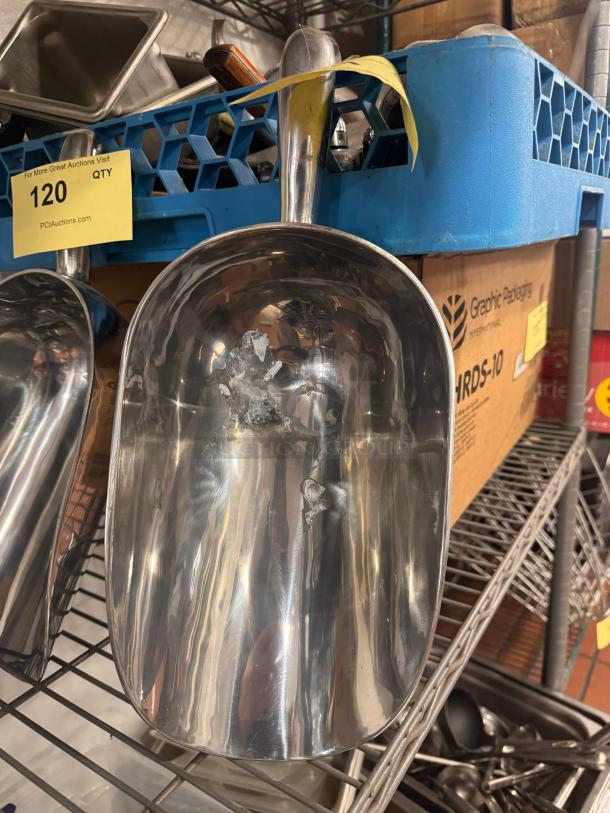 Stainless steel ice scoop with a curved handle, reflecting light. Visible wear on surface, resting on a blue crate.