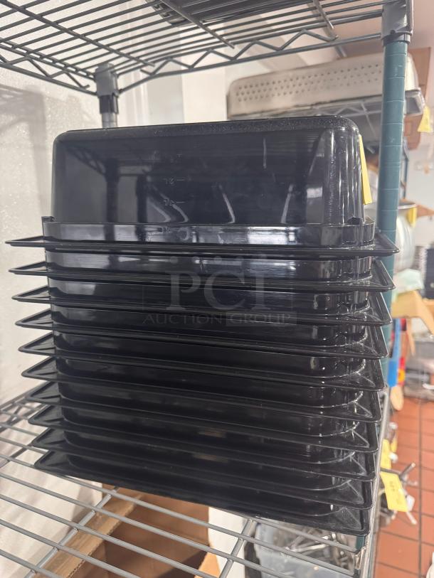 Stack of black plastic food pans, model BIDX10, in good condition on metal shelving.