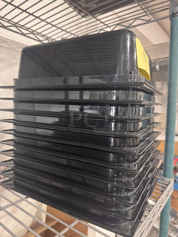 Stack of black plastic food pans, model BIDX10, in good condition on a metal shelf.