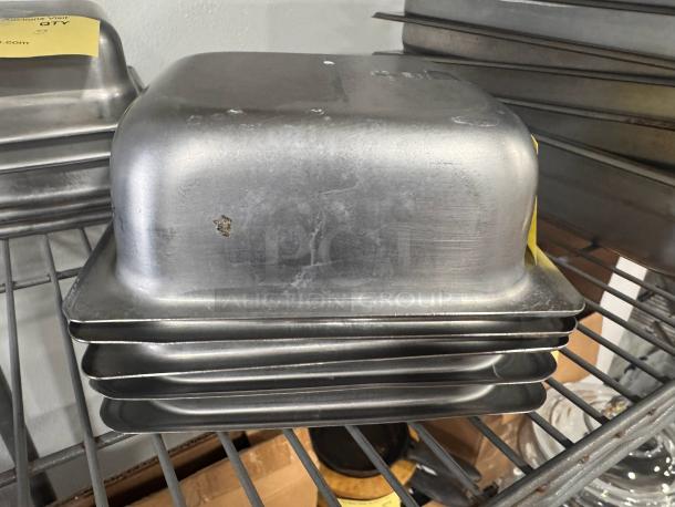Stainless steel food pan BIDX5, stack of four, used condition with minor scratches, visible on metal shelving.