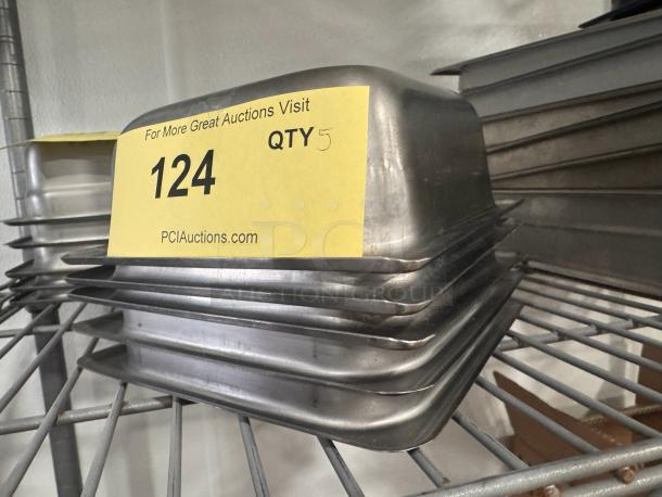Stainless steel food pans BIDX5, stack of five, on metal shelf. Label reads "124 QTY 5" from PCI Auctions.