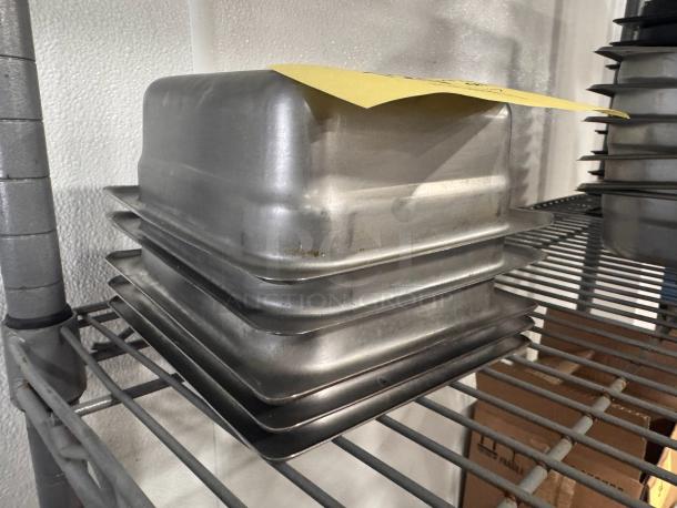 Stainless steel food pan BIDX5, stackable, good condition, on metal shelf. Features durable construction and minor wear.