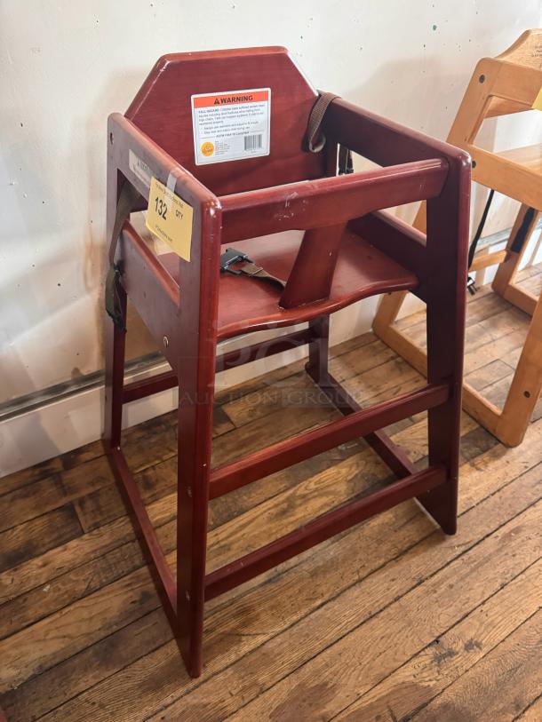 Wood high chair with safety straps, rich brown finish, and visible wear. Includes manufacturer warning label and auction tag.