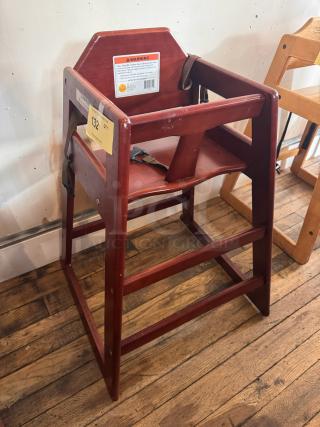 Wood high chair with safety straps, rich brown finish, and visible wear. Includes manufacturer warning label and auction tag.