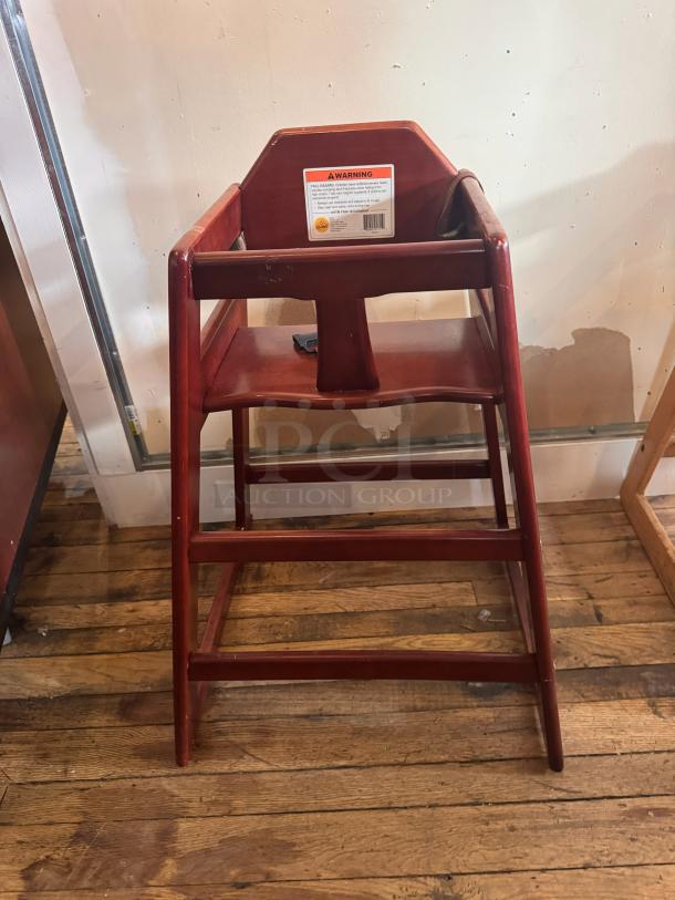 Wooden high chair with a rich brown finish. Features a sturdy design, safety harness, and visible safety warning label on the back.