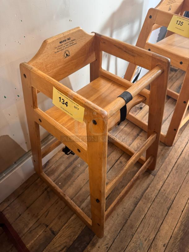 Wooden high chair with safety strap, natural finish, sturdy construction, moderate wear. Label warning for child safety. Auction tag 134.