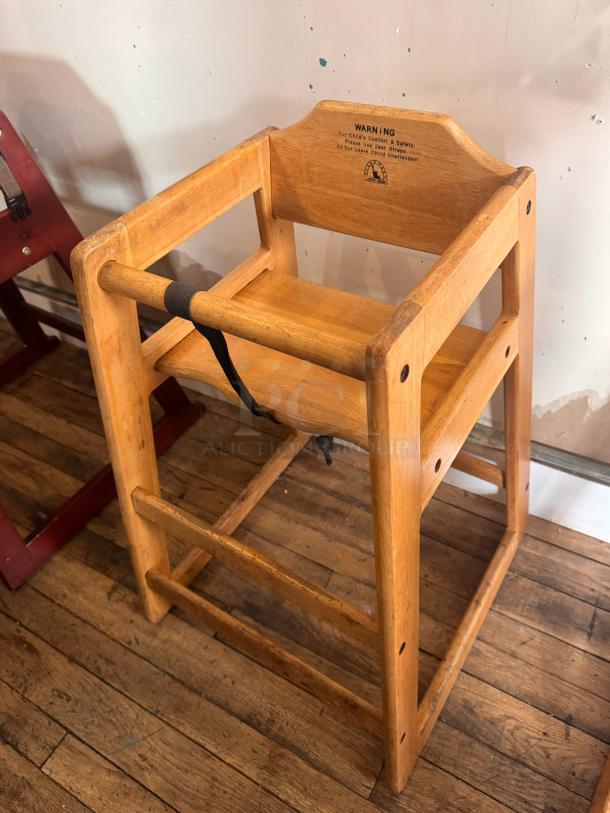 Wooden high chair with safety strap, sturdy design. Features warning label for child's safety. Good condition.
