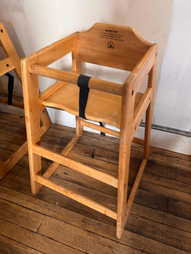 Wooden high chair with a protective black strap, natural finish, and visible safety warning label in good condition.