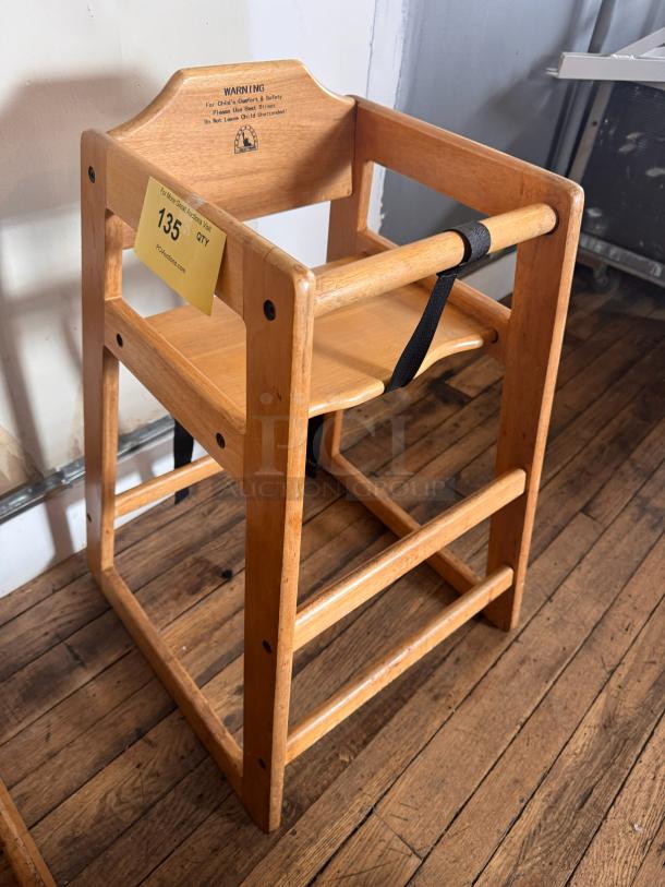 Wood high chair with natural finish, harness strap, and warning label for child safety. Item tag reads "135."