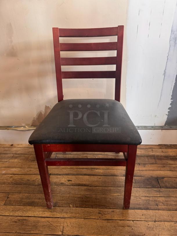 Wooden dining chair BIDX3, ladder-back design, with a black cushioned seat. Shows wear on legs and seat.