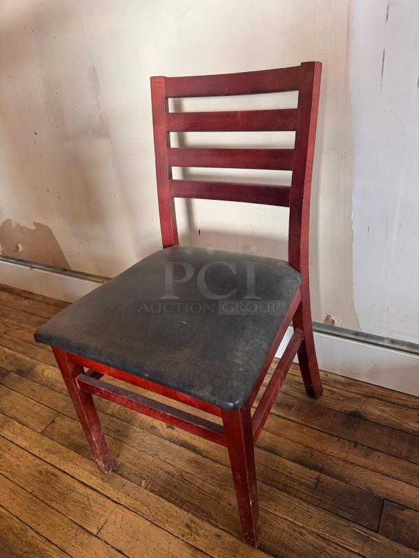 Wooden dining chair BIDX3 with red finish, ladder-back design, and black cushioned seat. Visible scratches, used condition.