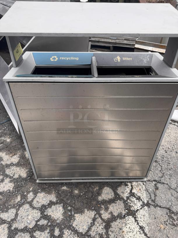 Stainless steel recycling receptacle with separate compartments for recycling and litter. Outdoor use, visible wear.