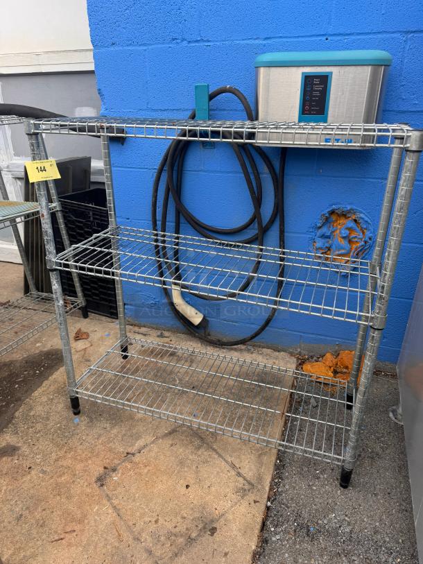 Metallic 36" wire shelf, three tiers, sturdy build, outdoor setting, industrial style, minor wear. Auction tag visible.