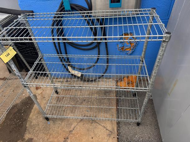 36" metal wire shelf with three tiers and adjustable feet, used condition. Auction tag 144 attached.