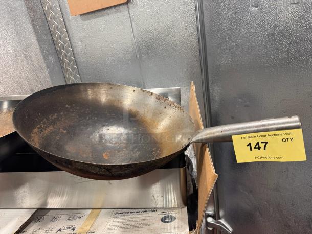 Steel wok with visible wear and rust, featuring a long handle. Auction label reads "147" from PCI Auctions.