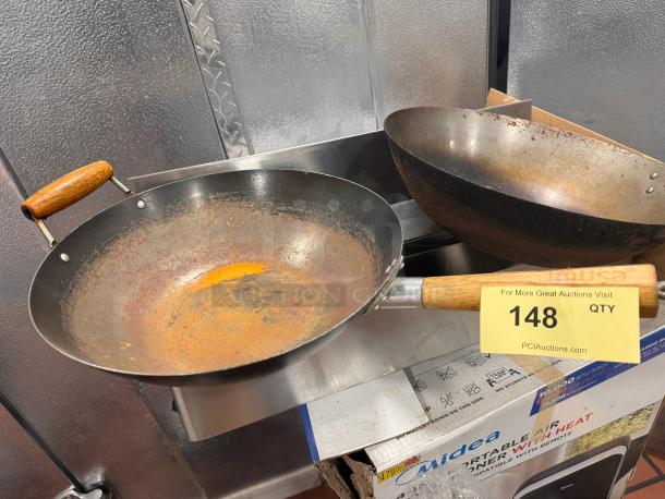 Steel wok with wooden handle, showing signs of rust. Includes auction tag labeled "148" on the handle.