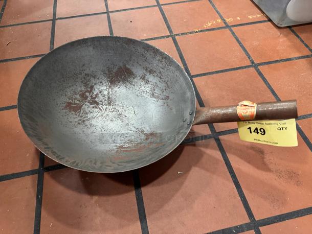 Rustic metal wok with wooden handle, showing wear. Attached auction label with number 149, indicating item for auction.