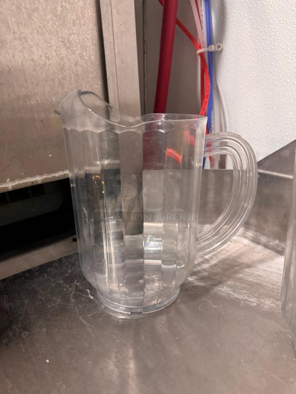 Clear plastic pitcher BIDX2 with a ribbed design and sturdy handle, in good condition. Suitable for beverages.