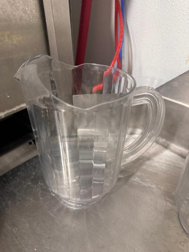 Clear plastic pitcher with ribbed design, sturdy handle, and spout. In good condition. Ideal for casual dining use.