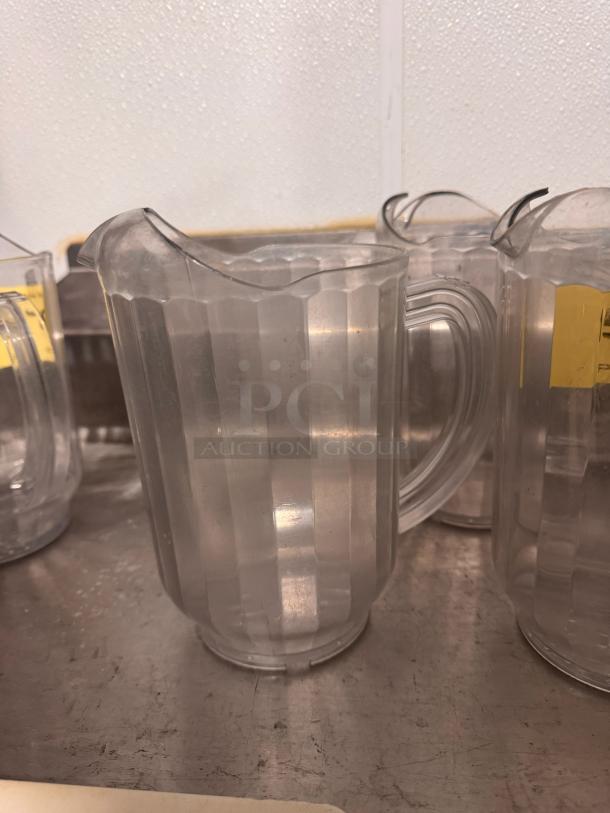 Clear plastic pitcher BIDX3 with a ribbed design, spout, and handle. Shows slight wear. Ideal for beverages.