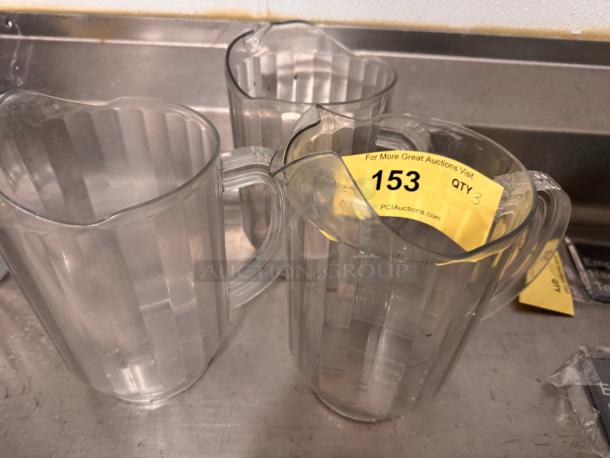 Three clear plastic pitchers with ridged design, used condition. Auction tag reads "153, QTY 3, PCIAuctions.com".
