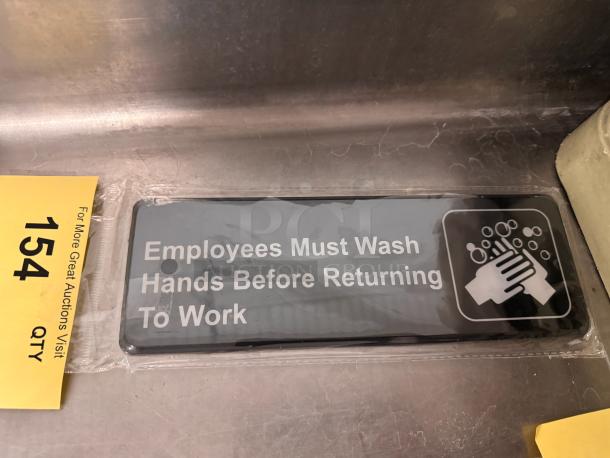 Brand new black and white sign reading "Employees Must Wash Hands Before Returning to Work," packaged in plastic.