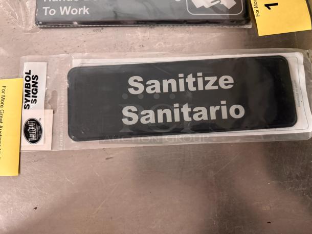 Brand new "Sanitize/Sanitario" sign by TableCraft, in packaging. Black with white text. From Symbol Signs series.