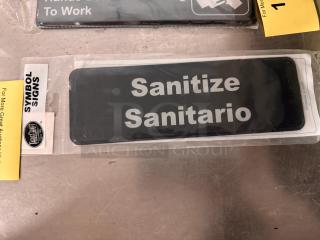 Brand new "Sanitize/Sanitario" sign by TableCraft, in packaging. Black with white text. From Symbol Signs series.