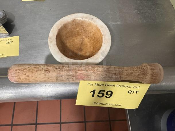 A marble mortar and wooden pestle on a metal surface. Item label indicates auction number 159. Slight wear visible.