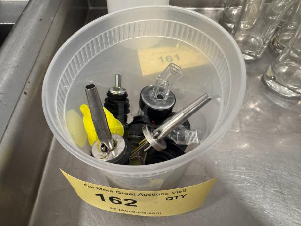 Lot of assorted pour spouts in a plastic container; includes metal and plastic types. Condition appears used. Auction tag no. 162.