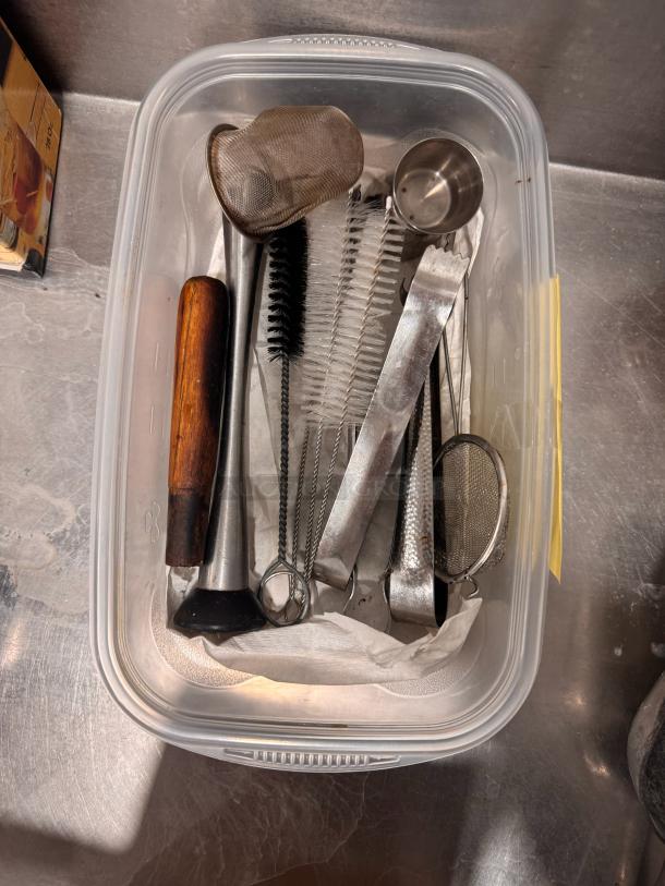 Bar tools set in a plastic container, includes a muddler, strainers, jigger, and cleaning brushes. Mixed materials; used condition.