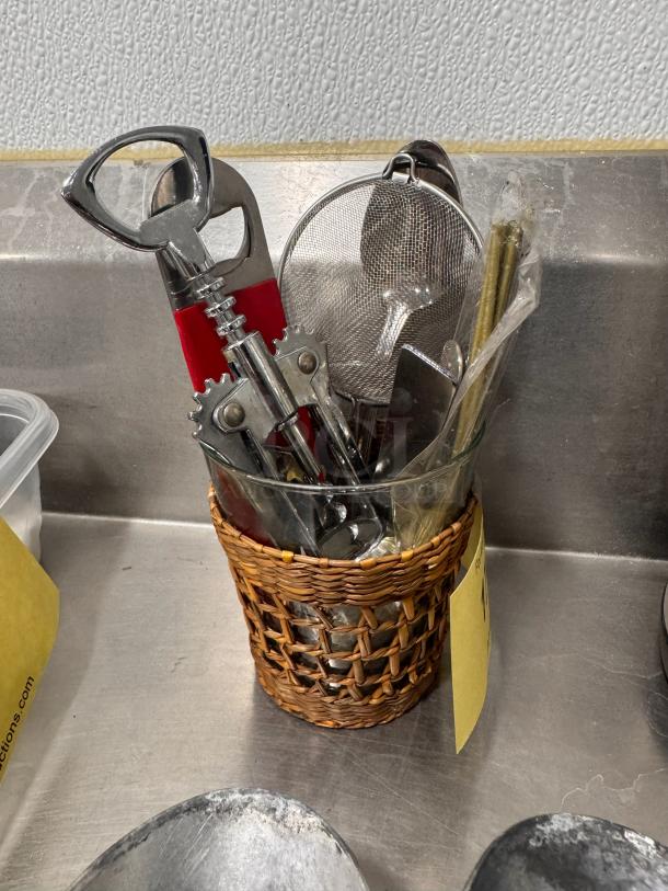 Lot of miscellaneous bar tools in a woven basket, includes corkscrew, strainer, and opener. Good condition.